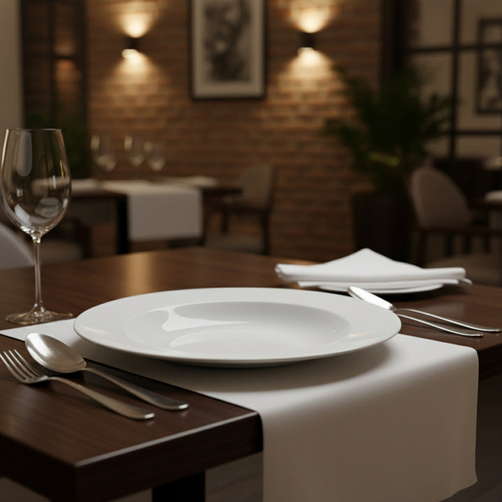 Dining table setting with white plates, silverware, and a glass in a restaurant.