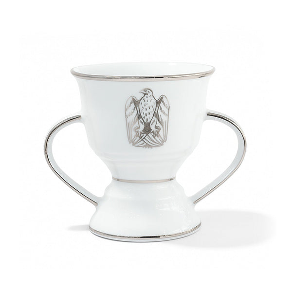 White ceramic cup with silver handles and a central emblem on a white background