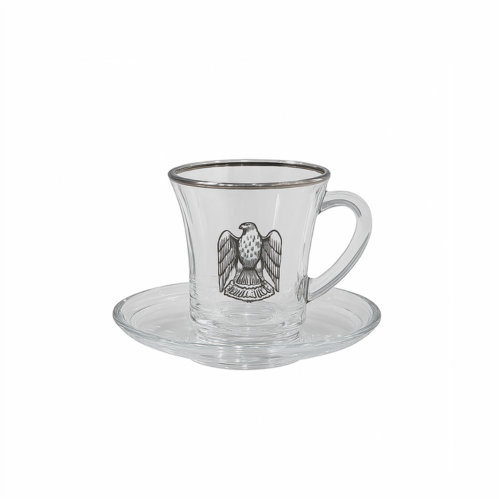 Clear glass cup and saucer with an eagle emblem on a white background