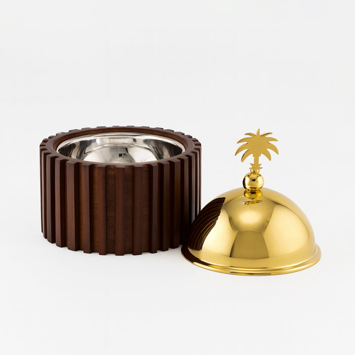 Brown textured container with a silver interior next to a gold bell with a palm tree design on a white background