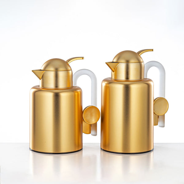 Two gold-colored oil dispensers with white handles on a white background