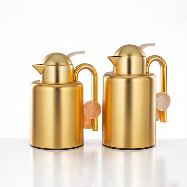 Two gold-colored oil and vinegar dispensers on a white background