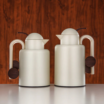 Two cream-colored ceramic teapots with wooden accents on a wooden surface.