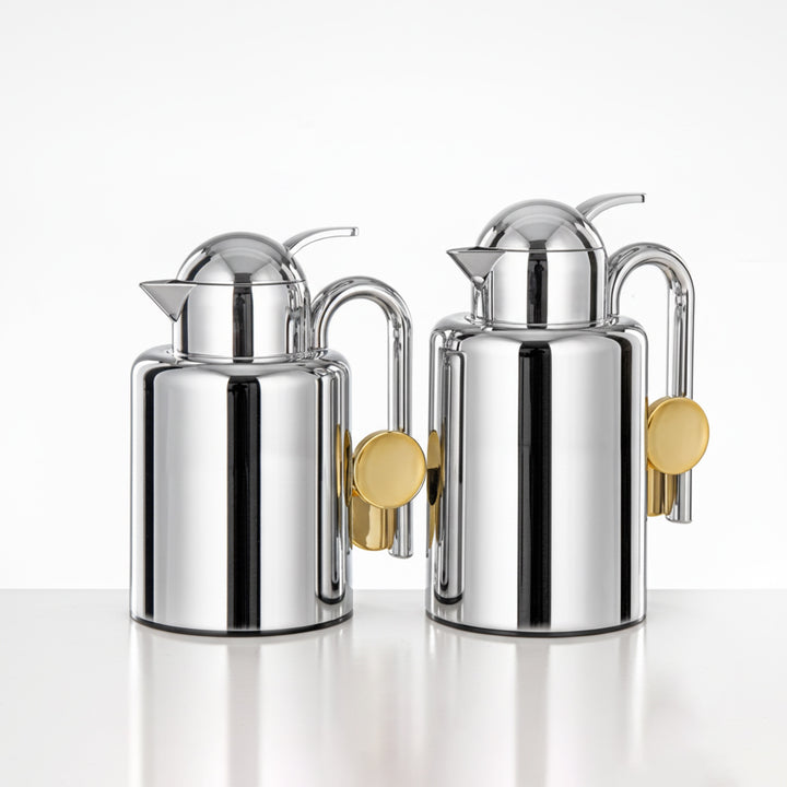 Two silver milk jugs with gold accents on a white background