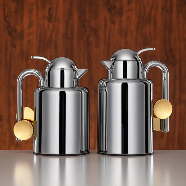 Two silver milk jugs with gold accents on a white background
