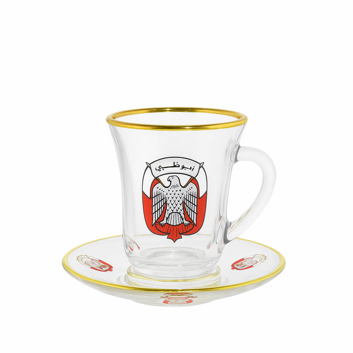 Clear glass mug with gold rim and red emblem on a matching saucer, on a white background