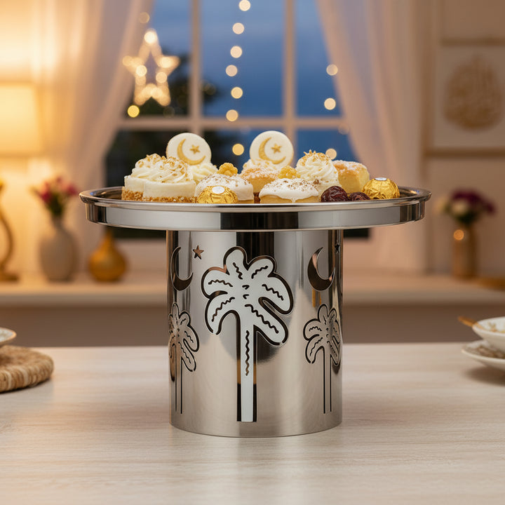 Decorative metal cake stand with palm tree designs on a table with a blurred festive background.