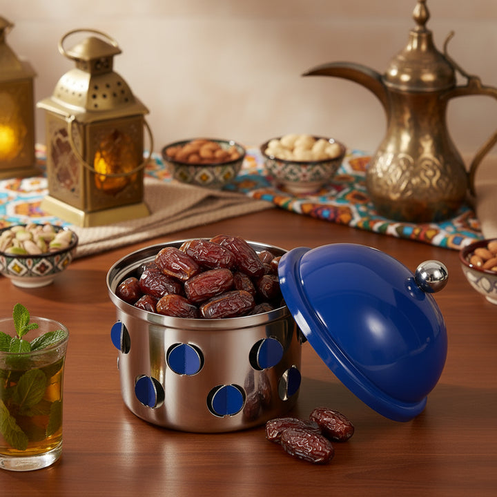 Container with blue polka dot lid filled with dates on a wooden table with tea and snacks.