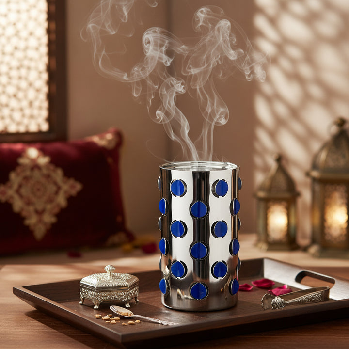 Decorative diffuser with blue polka dots on a wooden tray with candles and a pillow in the background.