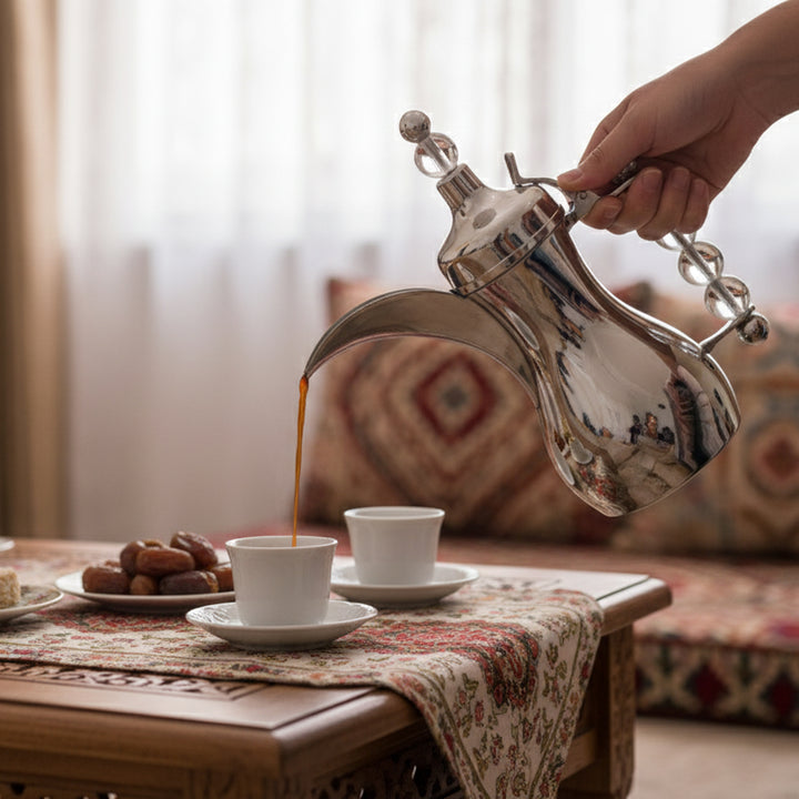 Person pouring coffee from a silver French press into a white cup on a wooden table.