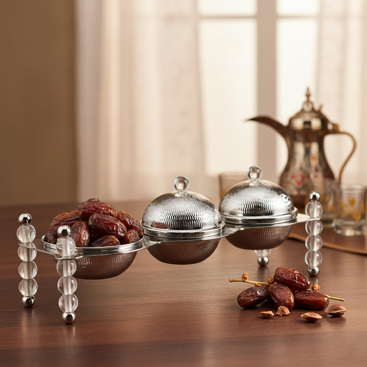 Decorative metal trays with crystal handles on a wooden surface, surrounded by dates.