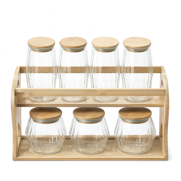 Set of glass jars with wooden lids on a wooden rack against a white background