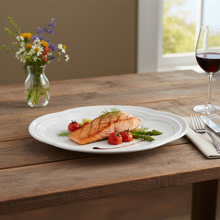 Salmon dish on a white plate with vegetables on a wooden table, accompanied by a glass of red wine and a vase of flowers.