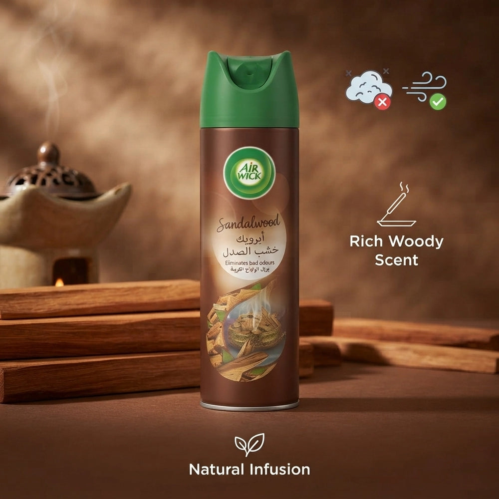 A can of Air Wick Sandalwood room spray in a rich woody scent, set against a warm, rustic background with wooden props and a teapot. The can features a green spray top and a brown body with a ship illustration near the bottom.