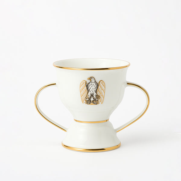 White ceramic cup with gold accents and an eagle emblem on a white background
