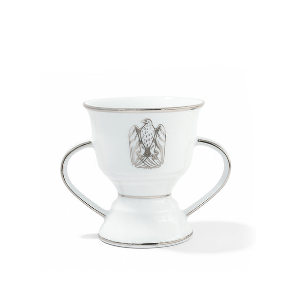 White ceramic cup with silver handles and a central emblem on a white background