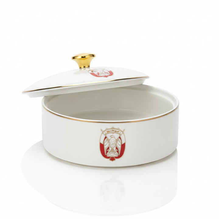 White ceramic dish with gold rim and red emblem on a white background