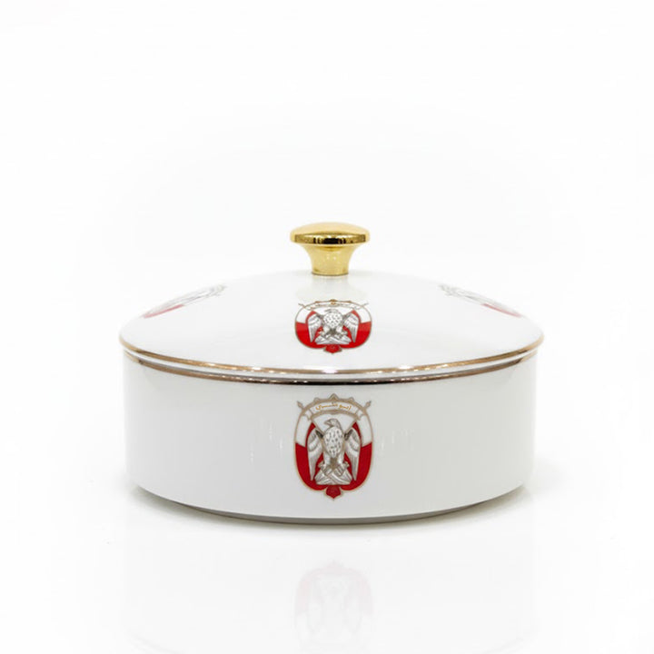 White ceramic dish with gold rim and red emblem on a white background