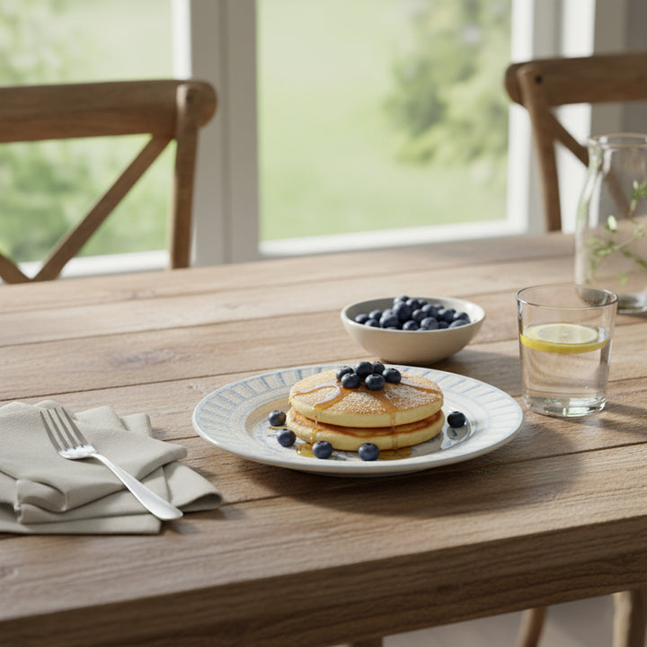 Stack of pancakes with blueberries on a plate, served with a glass of water and a bowl of blueberries on a wooden table.