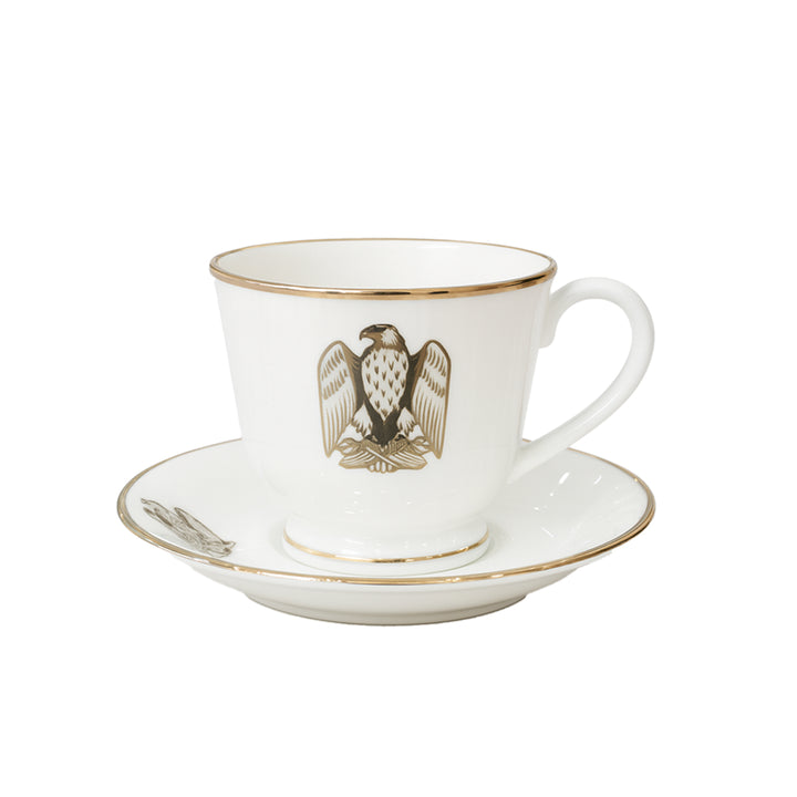 White teacup and saucer set with gold rim and eagle emblem on a white background