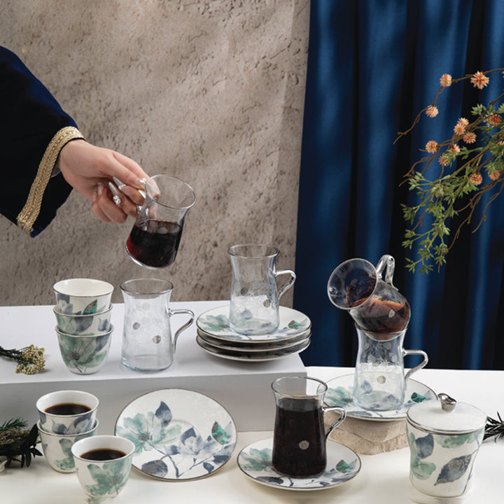 Tea-making setup with cups, saucers, and a teapot on a table against a neutral wall.