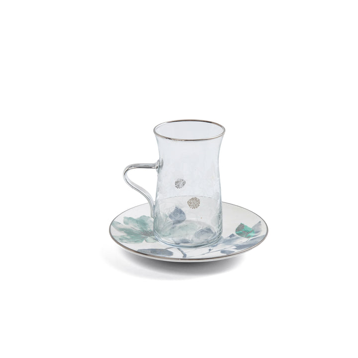 Clear glass cup with floral design on a matching saucer on a white background
