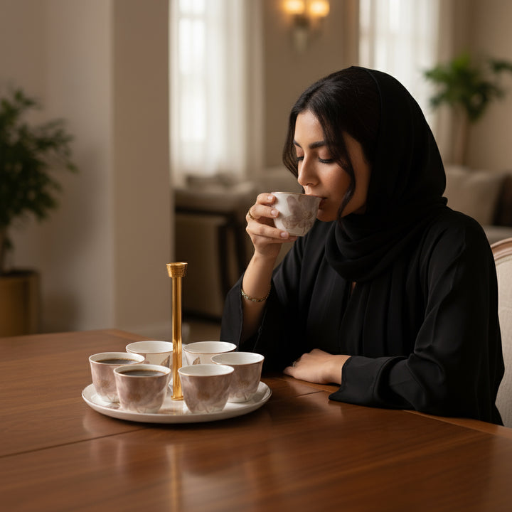 Woman in black hijab drinking from a cup with a tray of tea on a wooden table.