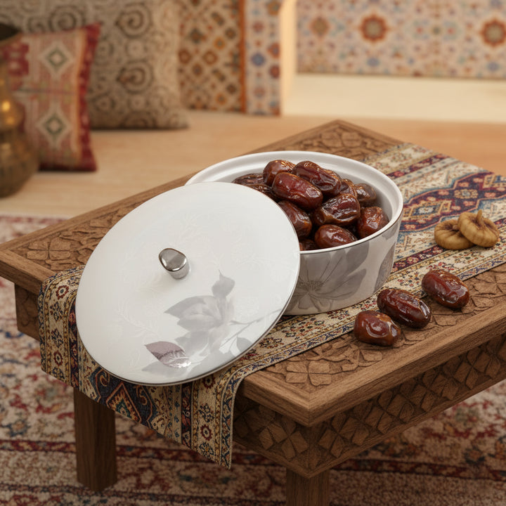 Ceramic dish with dates on a wooden table with a patterned rug and cushions in the background