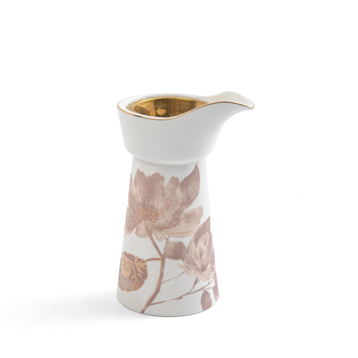 White ceramic creamer with floral design and gold accents on a white background