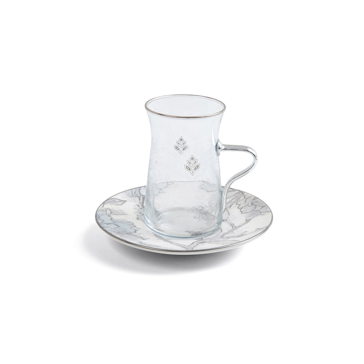 Clear glass teacup with handle and decorative saucer on a white background