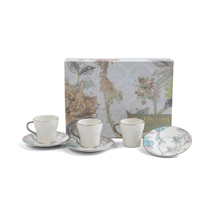 Ceramic tea set with three cups and saucers in front of a decorative box on a white background