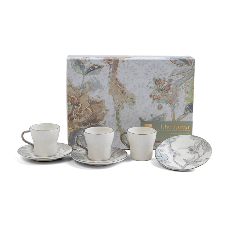 Ceramic tea set with saucers and cups in front of a decorative box on a white background