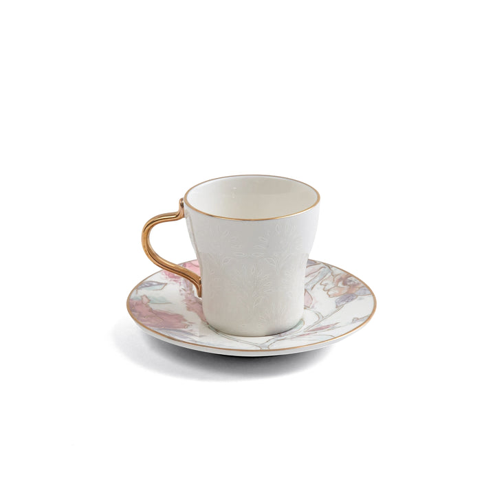White ceramic cup with gold handle on a matching saucer with floral design on a white background