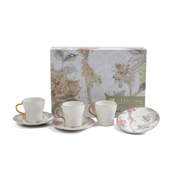 Set of three ceramic cups and saucers with floral design in front of a decorative box, on a white background.