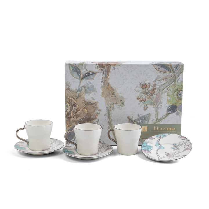Tea set with cups, saucers, and a plate in front of a floral-patterned box on a white background