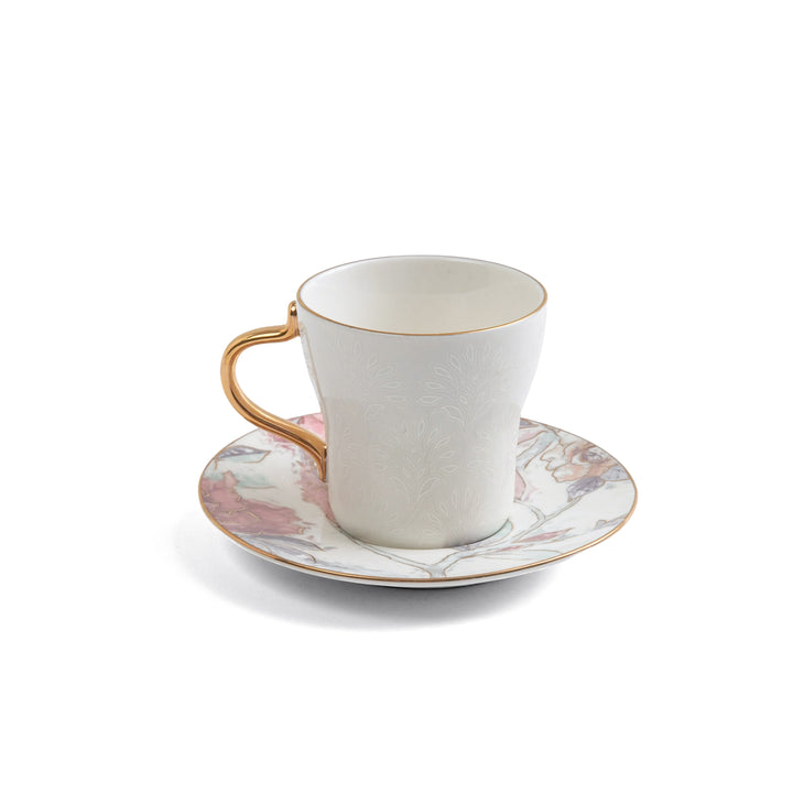 White ceramic cup with gold handle and saucer with floral design on a white background