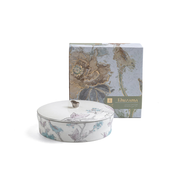 Decorative ceramic lidded dish with floral design next to its packaging on a white background
