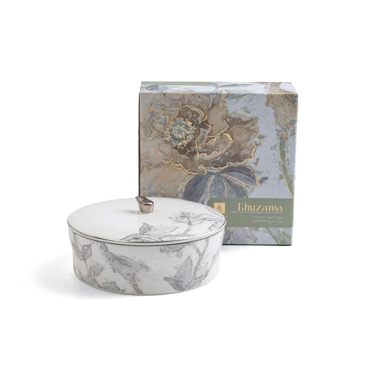Decorative candle with floral design in front of a matching box on a white background
