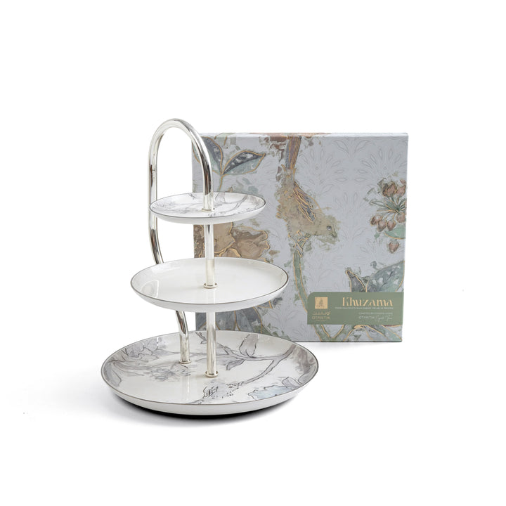 Three-tiered ceramic serving tray with floral design in front of a branded box on a white background