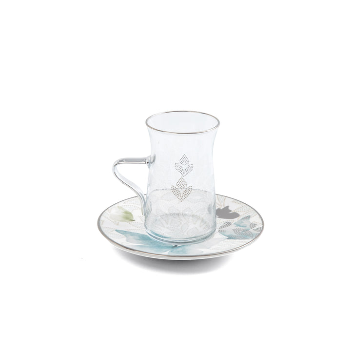 Clear glass cup with decorative handle on a matching saucer with floral design on a white background