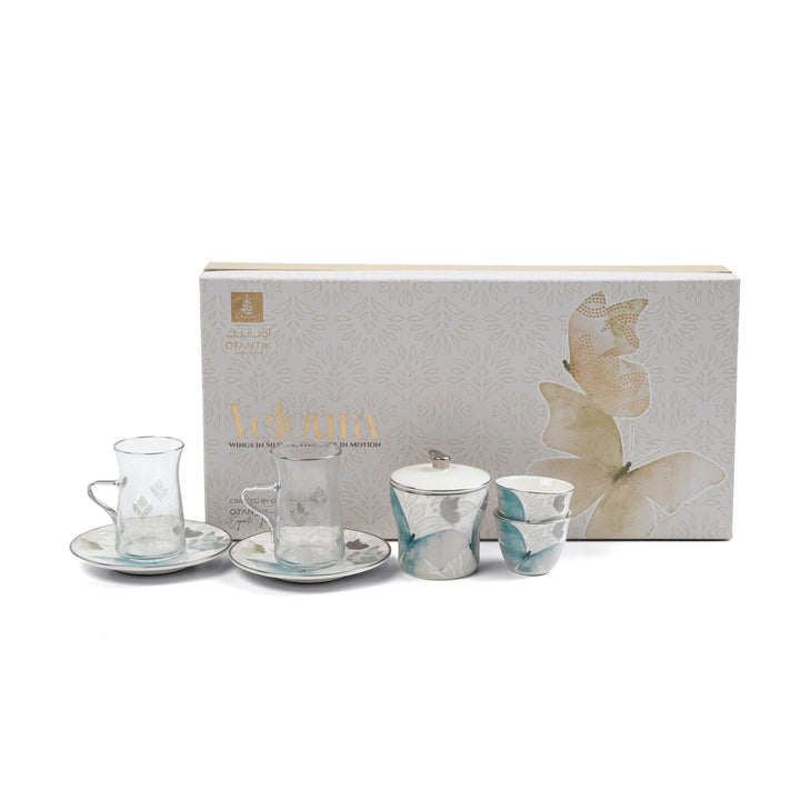 Tea set with glass cups and saucers in front of a branded box on a white background