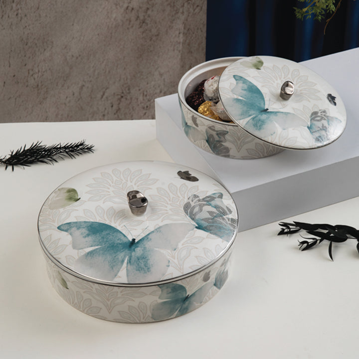 Round decorative containers with butterfly designs on lids on a white surface.