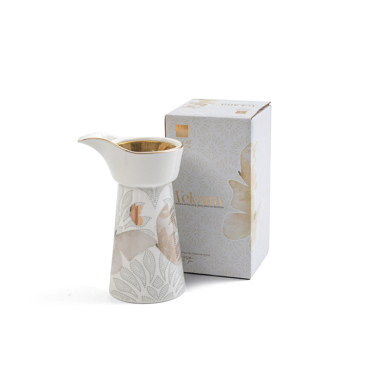 Ceramic creamer with floral design next to its packaging on a white background