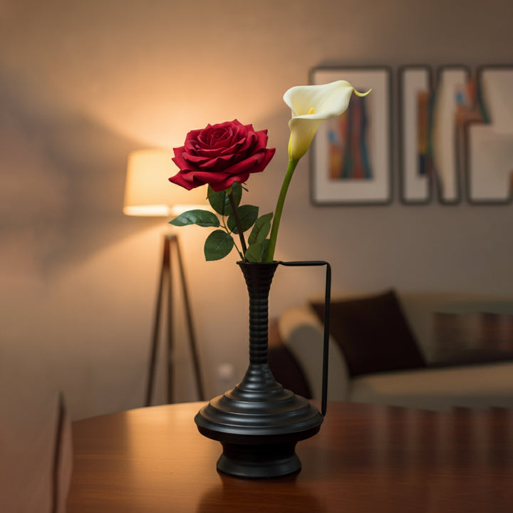 Vase with a red rose and white calla lily on a wooden table in a softly lit room.