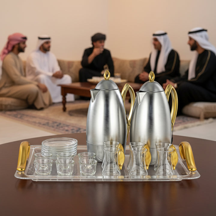 Silver and gold teapot set on a tray with people in traditional attire in the background.