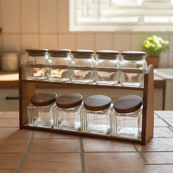 Glass spice jars with wooden lids in a wooden holder on a kitchen counter.