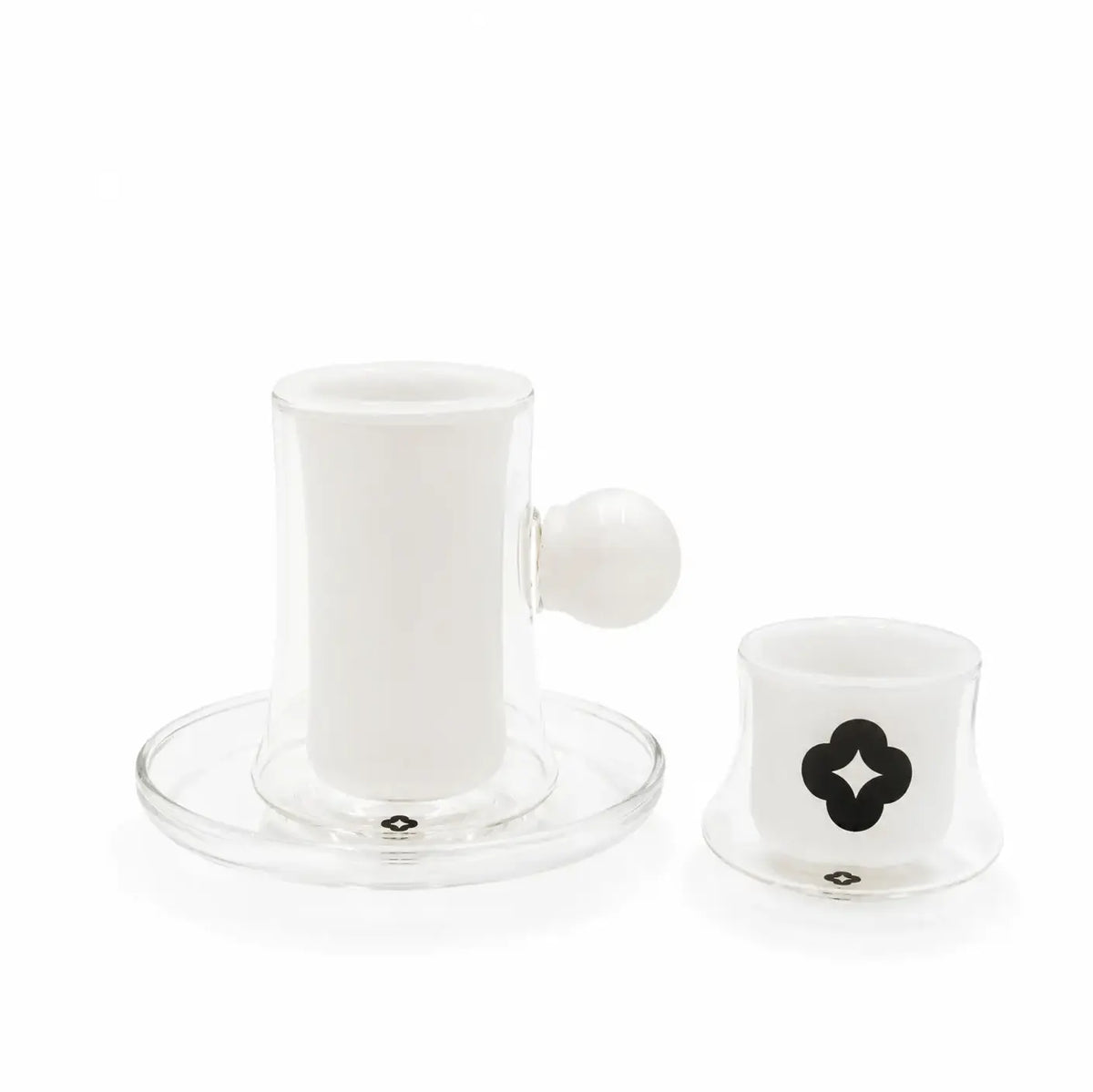A clear glass coffee maker set with a white ceramic inner cup and saucer, a matching small white cup with a black clover logo, and a white spherical handle, photographed on a white background.