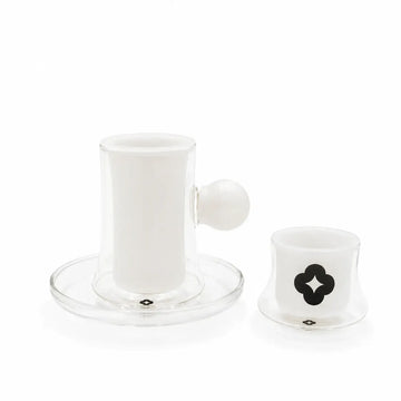 A clear glass coffee maker set with a white ceramic inner cup and saucer, a matching small white cup with a black clover logo, and a white spherical handle, photographed on a white background.