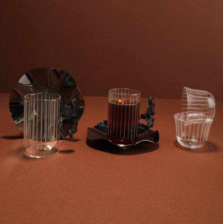 Set of glassware including a candle holder with a lit candle on a brown background