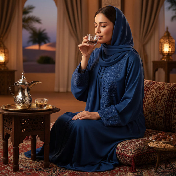 Woman in a blue dress drinking from a glass in a warm, decorated room.